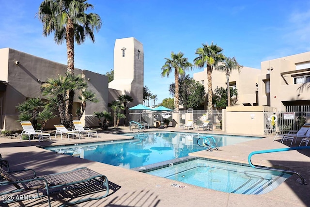 pool with a patio area, a community hot tub, and fence