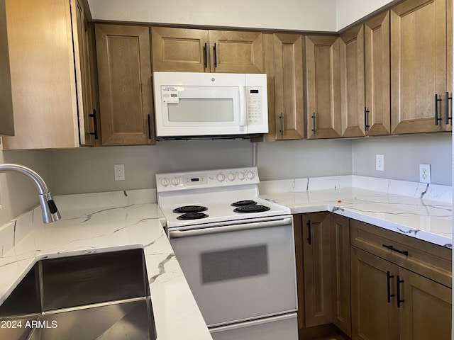 kitchen featuring light stone countertops, white appliances, and sink