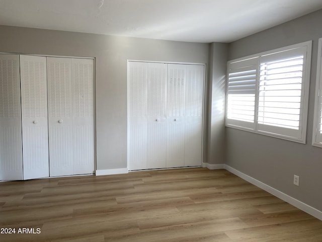 unfurnished bedroom with light hardwood / wood-style floors and multiple closets