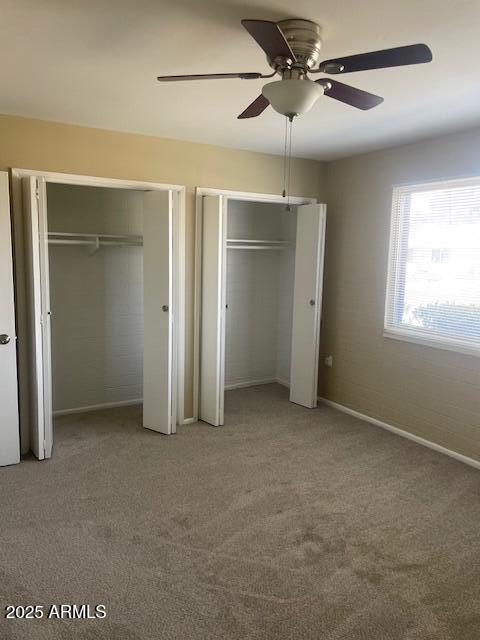 unfurnished bedroom featuring carpet flooring, two closets, and ceiling fan