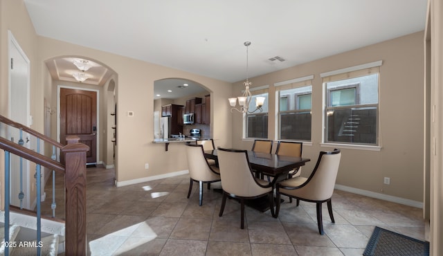 dining room with a chandelier, arched walkways, baseboards, and light tile patterned flooring