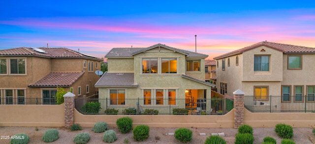 back of property at dusk with stucco siding and a tile roof