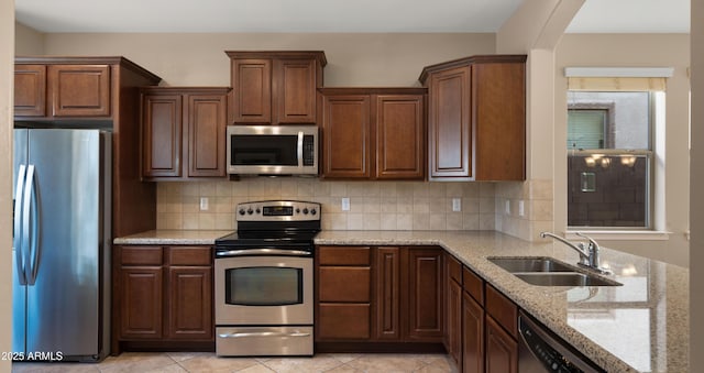 kitchen with appliances with stainless steel finishes, a sink, light stone counters, and backsplash