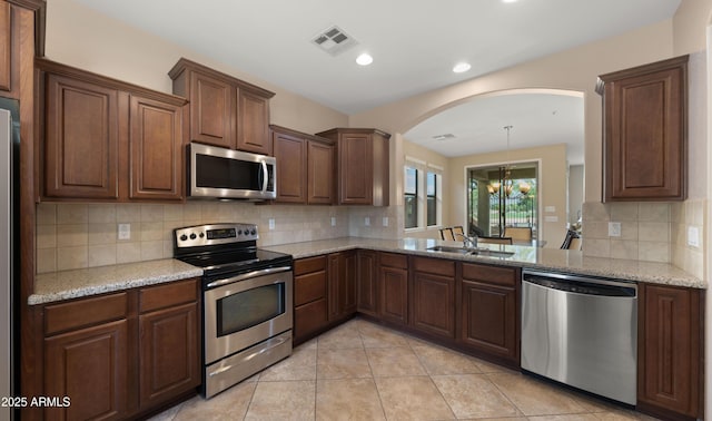 kitchen with appliances with stainless steel finishes, arched walkways, backsplash, a sink, and light tile patterned flooring