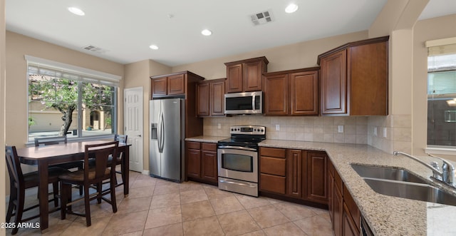 kitchen with appliances with stainless steel finishes, a sink, decorative backsplash, recessed lighting, and light stone countertops