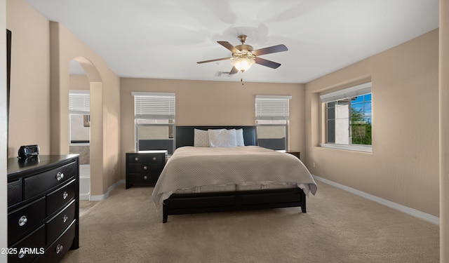 bedroom with baseboards, light carpet, a ceiling fan, and arched walkways