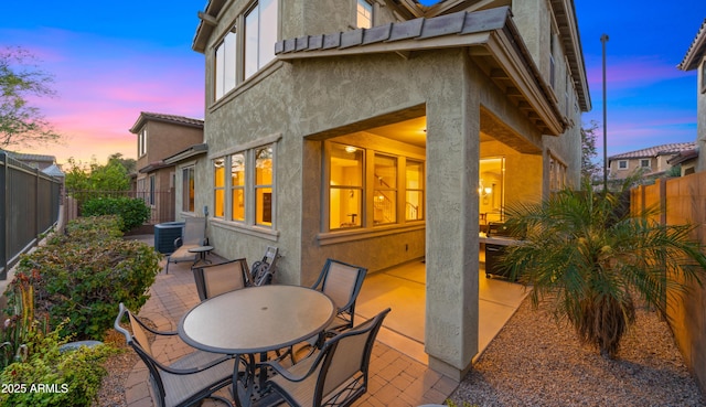 back of house at dusk featuring a patio, stucco siding, and a fenced backyard