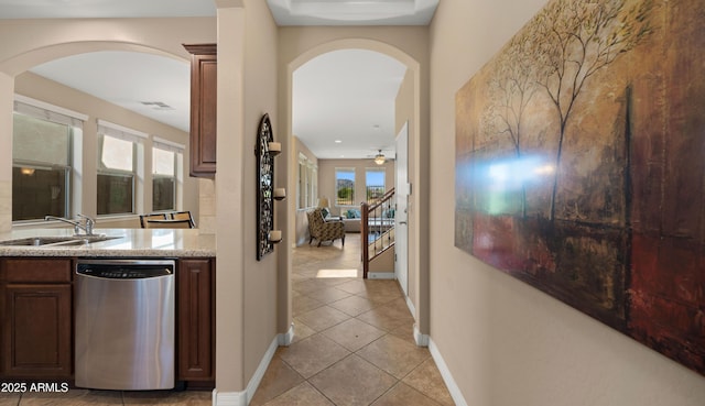 corridor with a sink, arched walkways, light tile patterned floors, and baseboards