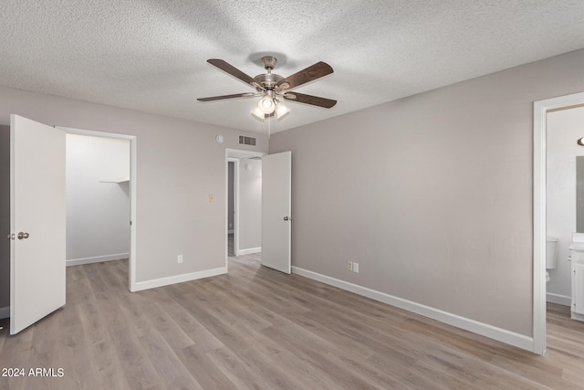 unfurnished bedroom with ceiling fan, a textured ceiling, light hardwood / wood-style flooring, a spacious closet, and ensuite bath