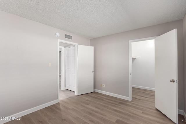 unfurnished bedroom featuring a textured ceiling, light hardwood / wood-style flooring, and a spacious closet