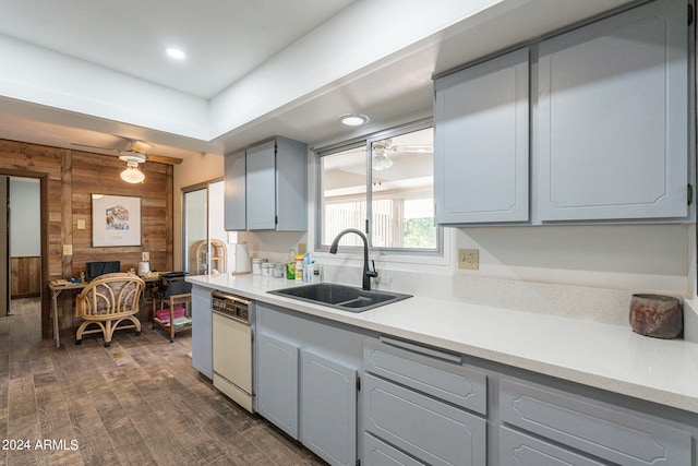 kitchen with wooden walls, sink, dark hardwood / wood-style flooring, white dishwasher, and gray cabinets