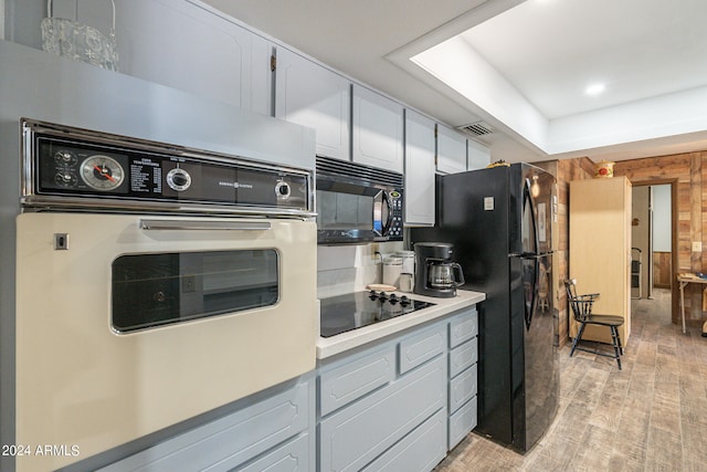 kitchen featuring light hardwood / wood-style flooring, wooden walls, white cabinets, and black appliances