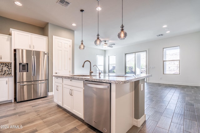 kitchen with ceiling fan, stainless steel appliances, pendant lighting, a kitchen island with sink, and white cabinets