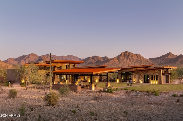 back house at dusk with a mountain view and a lawn