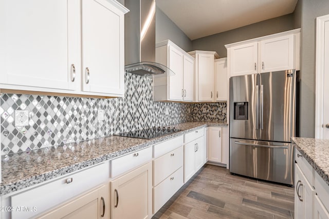 kitchen featuring stainless steel refrigerator with ice dispenser, black electric stovetop, wall chimney range hood, hardwood / wood-style flooring, and white cabinets