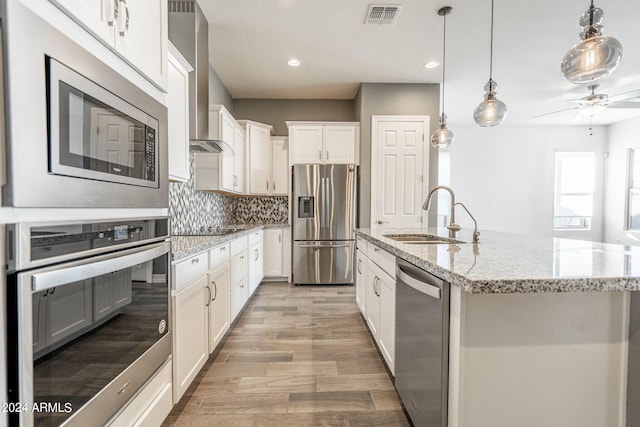 kitchen with a center island with sink, white cabinets, sink, wall chimney exhaust hood, and stainless steel appliances