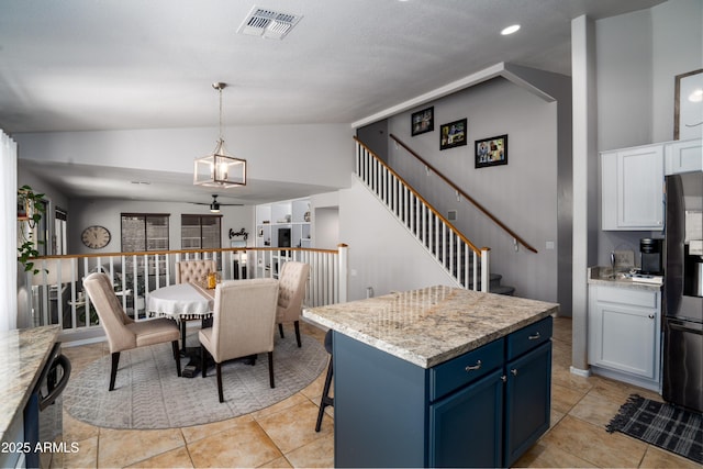 kitchen featuring black fridge, visible vents, vaulted ceiling, pendant lighting, and blue cabinets