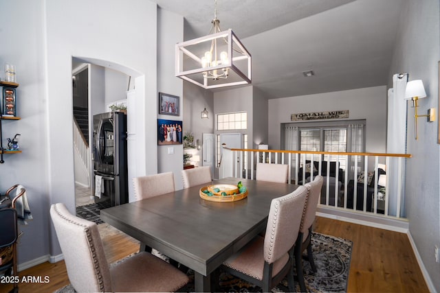 dining area featuring an inviting chandelier, stairs, wood finished floors, baseboards, and arched walkways