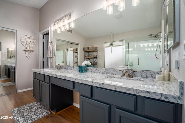 bathroom with double vanity, visible vents, a shower with shower door, wood finished floors, and a sink