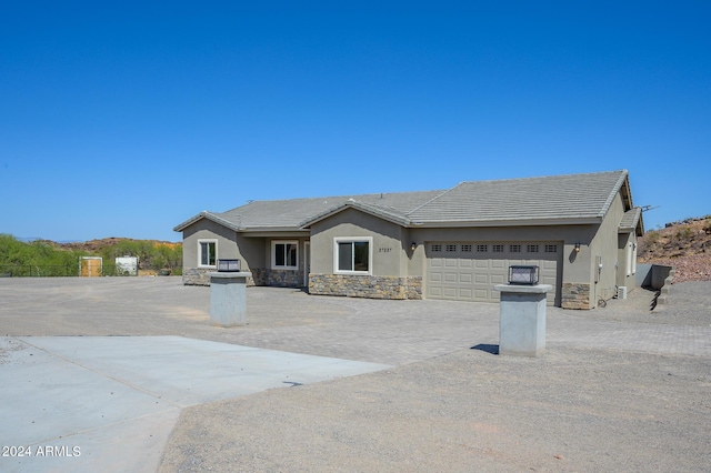 view of front facade featuring stucco siding, a garage, stone siding, driveway, and a tiled roof