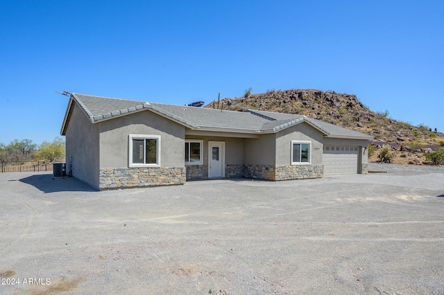 view of front facade featuring stucco siding, central AC unit, a garage, stone siding, and driveway