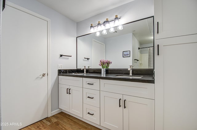 full bathroom featuring double vanity, a shower, a sink, and wood finished floors