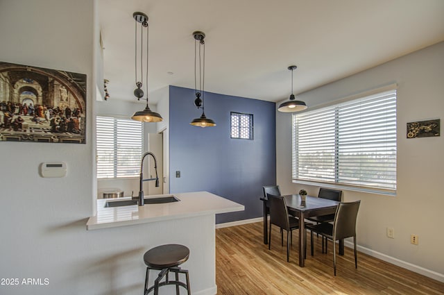 kitchen with pendant lighting, a sink, light wood-type flooring, a peninsula, and baseboards