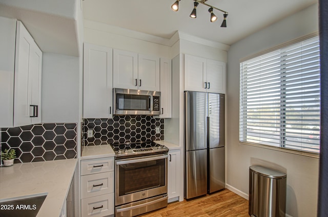 kitchen featuring stainless steel appliances, white cabinets, light wood-style floors, and backsplash