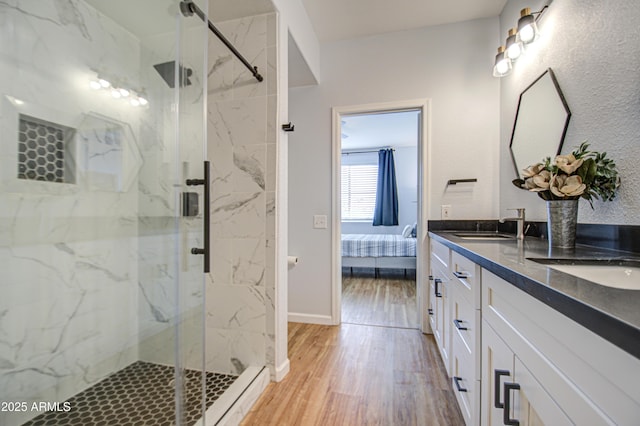 ensuite bathroom featuring a sink, double vanity, a marble finish shower, and wood finished floors