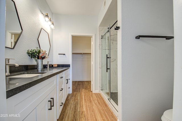 full bathroom with a marble finish shower, toilet, wood finished floors, a walk in closet, and vanity