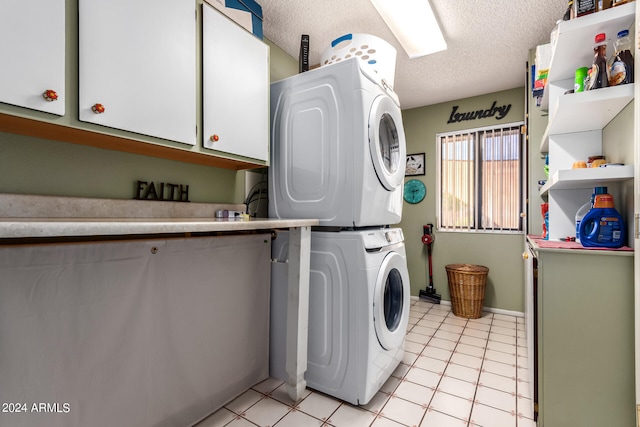 clothes washing area with a textured ceiling, light tile patterned floors, stacked washer and clothes dryer, and cabinets