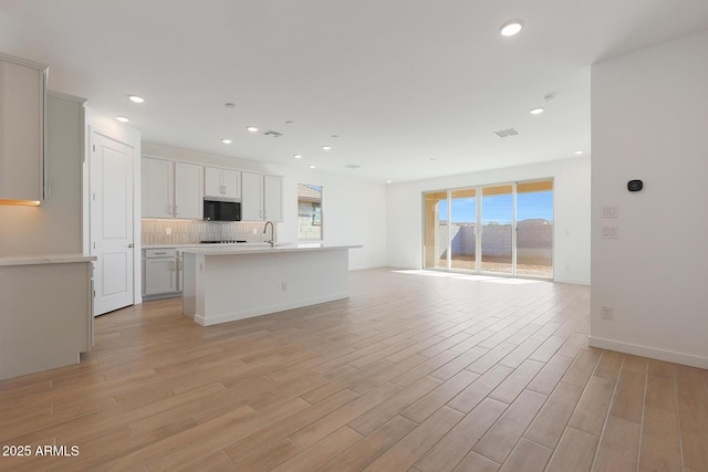 kitchen with sink, light wood-type flooring, a kitchen island with sink, and backsplash