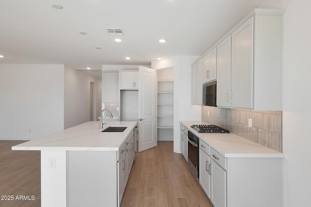 kitchen with stainless steel gas stovetop, wall oven, white cabinetry, a kitchen island with sink, and sink