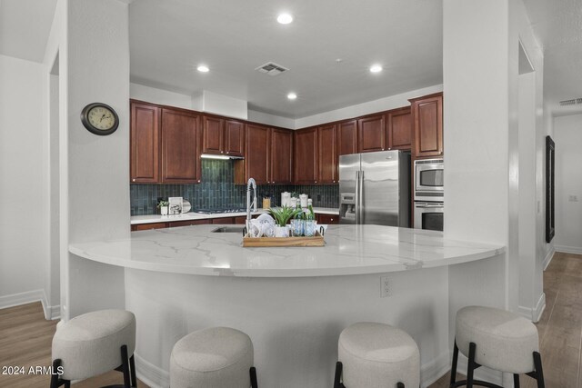 kitchen with light hardwood / wood-style floors, backsplash, kitchen peninsula, stainless steel appliances, and a kitchen bar