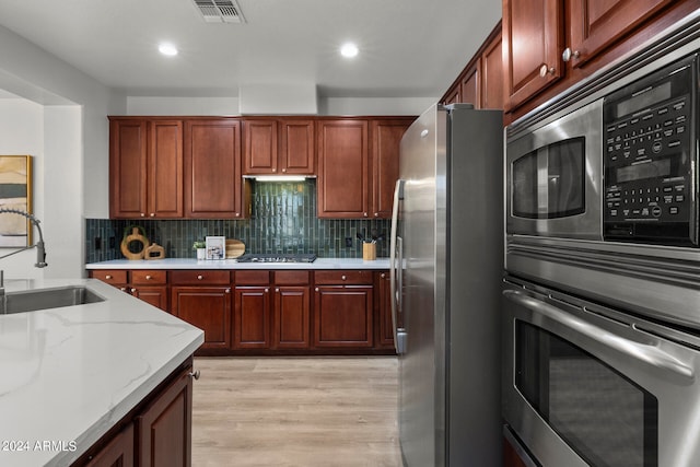 kitchen with stainless steel appliances, light wood-type flooring, sink, and tasteful backsplash