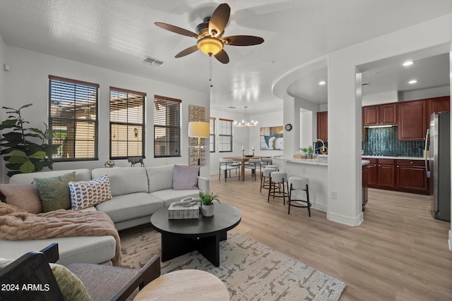 living room featuring ceiling fan with notable chandelier and light hardwood / wood-style flooring