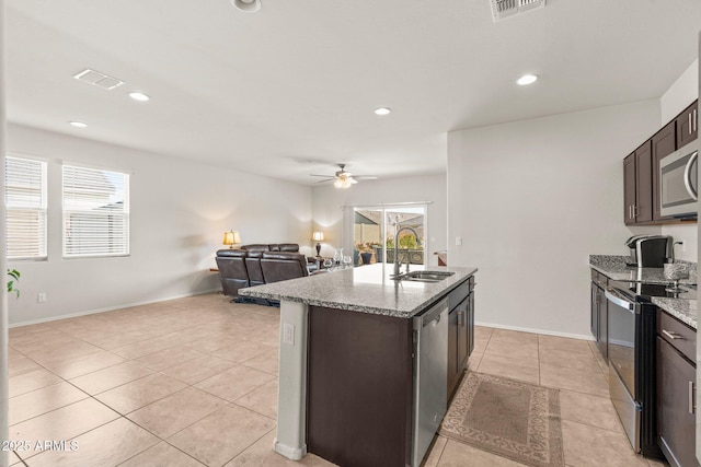 kitchen with sink, a center island with sink, light tile patterned floors, appliances with stainless steel finishes, and light stone countertops