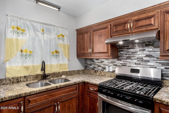 kitchen featuring backsplash, light stone countertops, under cabinet range hood, gas stove, and a sink