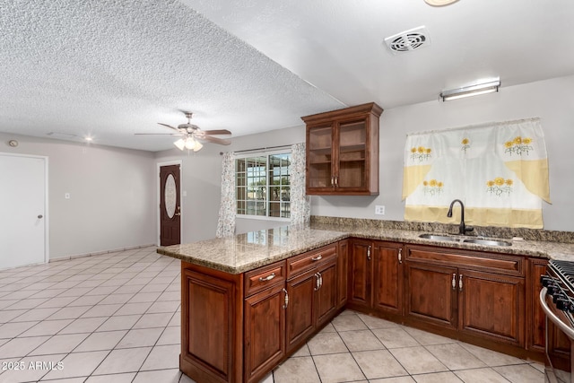 kitchen with a peninsula, light tile patterned floors, gas stove, and a sink