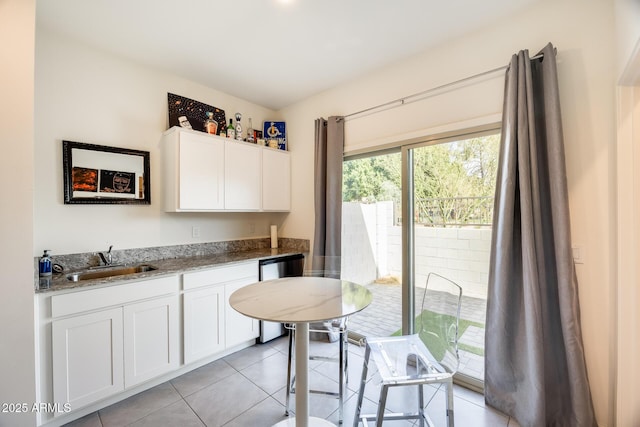 kitchen featuring light tile patterned floors, dishwashing machine, light stone counters, a sink, and white cabinetry