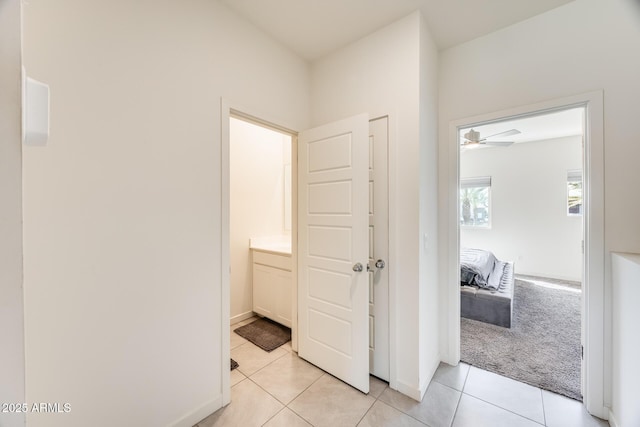 hall featuring light colored carpet, baseboards, and light tile patterned floors