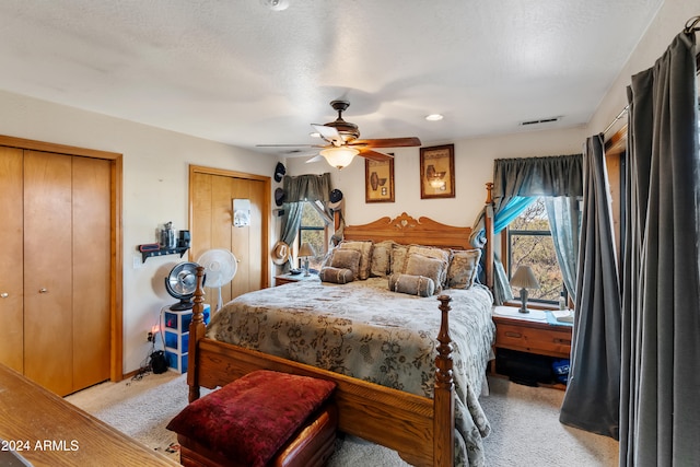 bedroom featuring ceiling fan, light colored carpet, a textured ceiling, and two closets