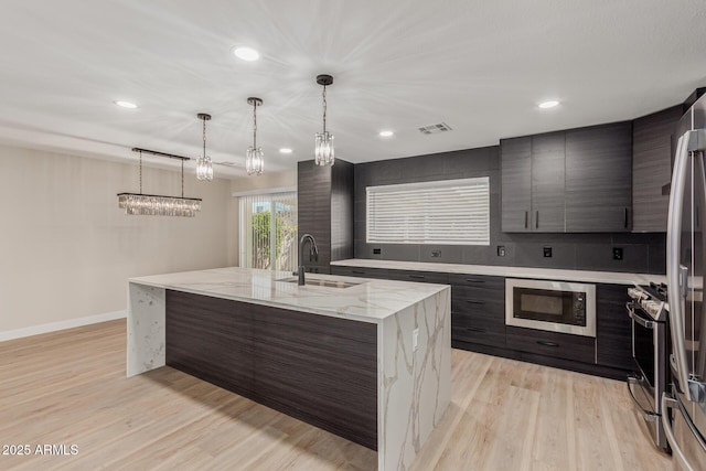 kitchen featuring sink, hanging light fixtures, light wood-type flooring, an island with sink, and stainless steel appliances