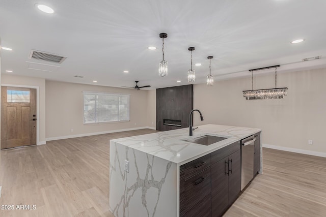 kitchen with an island with sink, sink, stainless steel dishwasher, and dark brown cabinetry