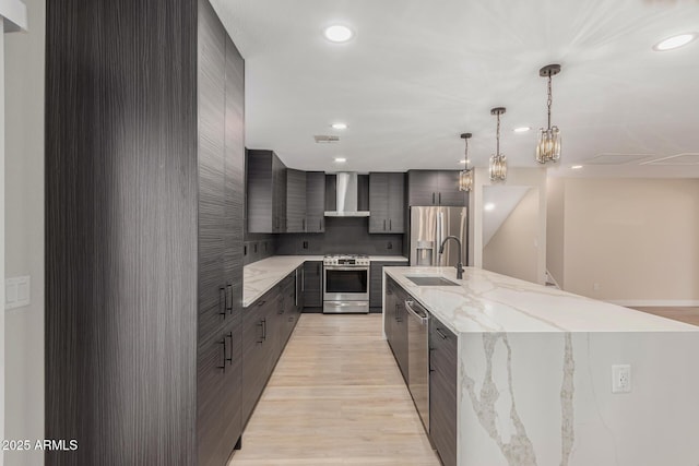 kitchen featuring wall chimney range hood, sink, light hardwood / wood-style flooring, appliances with stainless steel finishes, and decorative light fixtures