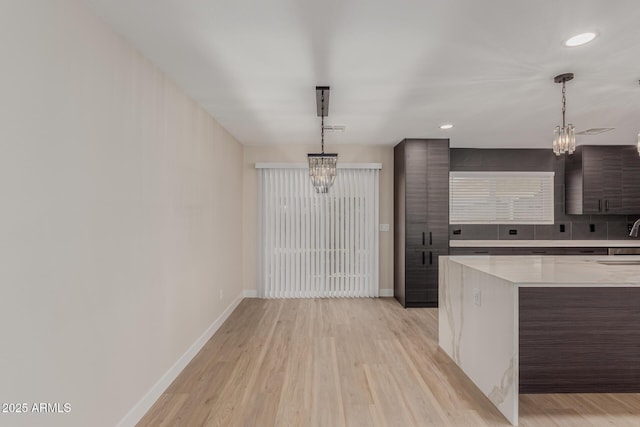 kitchen with light wood-type flooring, dark brown cabinets, a chandelier, and decorative light fixtures