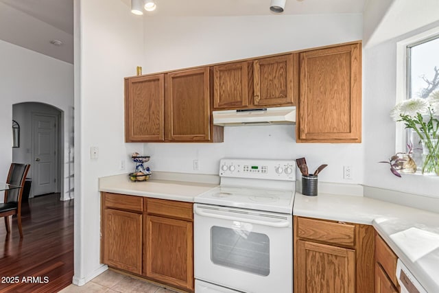 8566 N 108th Ln, Peoria, AZ 85345 - kitchen with white range with electric cooktop, under cabinet range hood, arched walkways, brown cabinetry, and light countertops