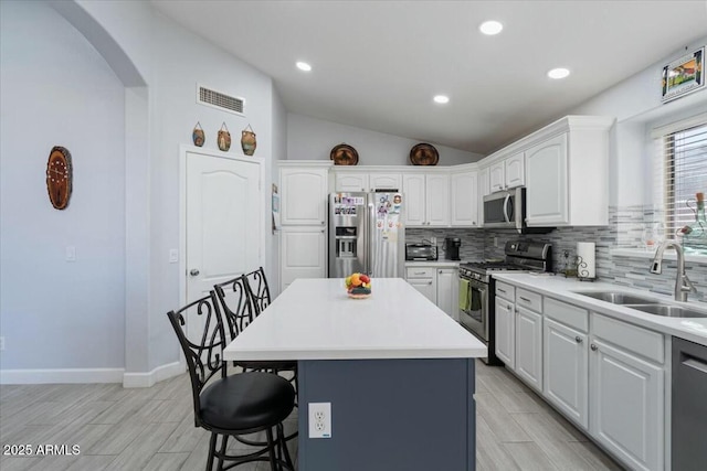 kitchen with vaulted ceiling, a kitchen island, white cabinetry, sink, and stainless steel appliances