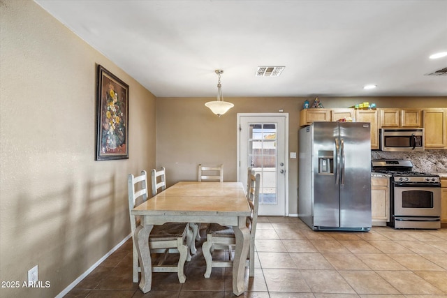 kitchen featuring light brown cabinetry, decorative light fixtures, light tile patterned floors, appliances with stainless steel finishes, and backsplash