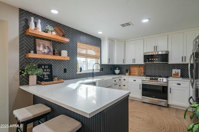 kitchen with sink, kitchen peninsula, white cabinets, and appliances with stainless steel finishes